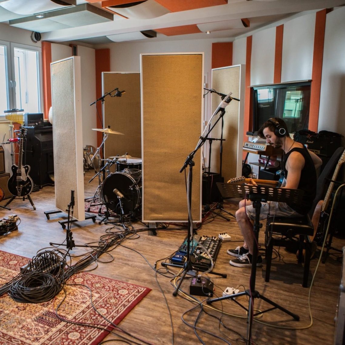 Musikaufnahme mit Drums, Gitarren und einem Musiker im Aufnahmestudio.